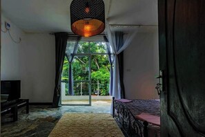 Ein Schlafzimmer mit Bett, Fernseher und Blick auf Grün hinter einer Glastür.