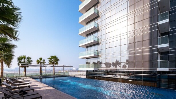 Ein modernes Hotel mit Dachpool, Palmen und Blick auf die Skyline der Stadt.