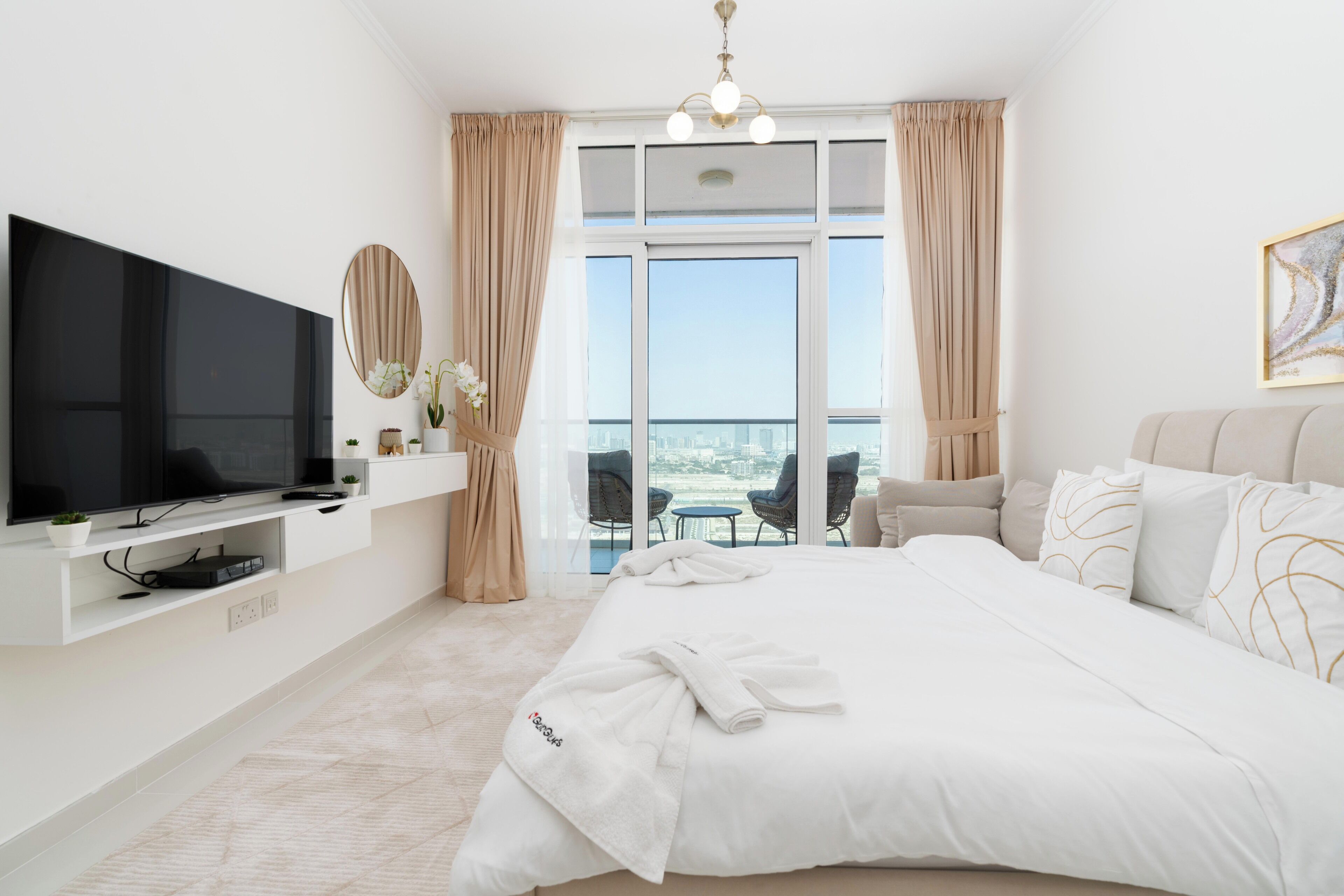 Camera d'albergo moderna con un ampio letto, una TV a schermo piatto, un balcone con vista sulla città e un'area ristoro con sedie.