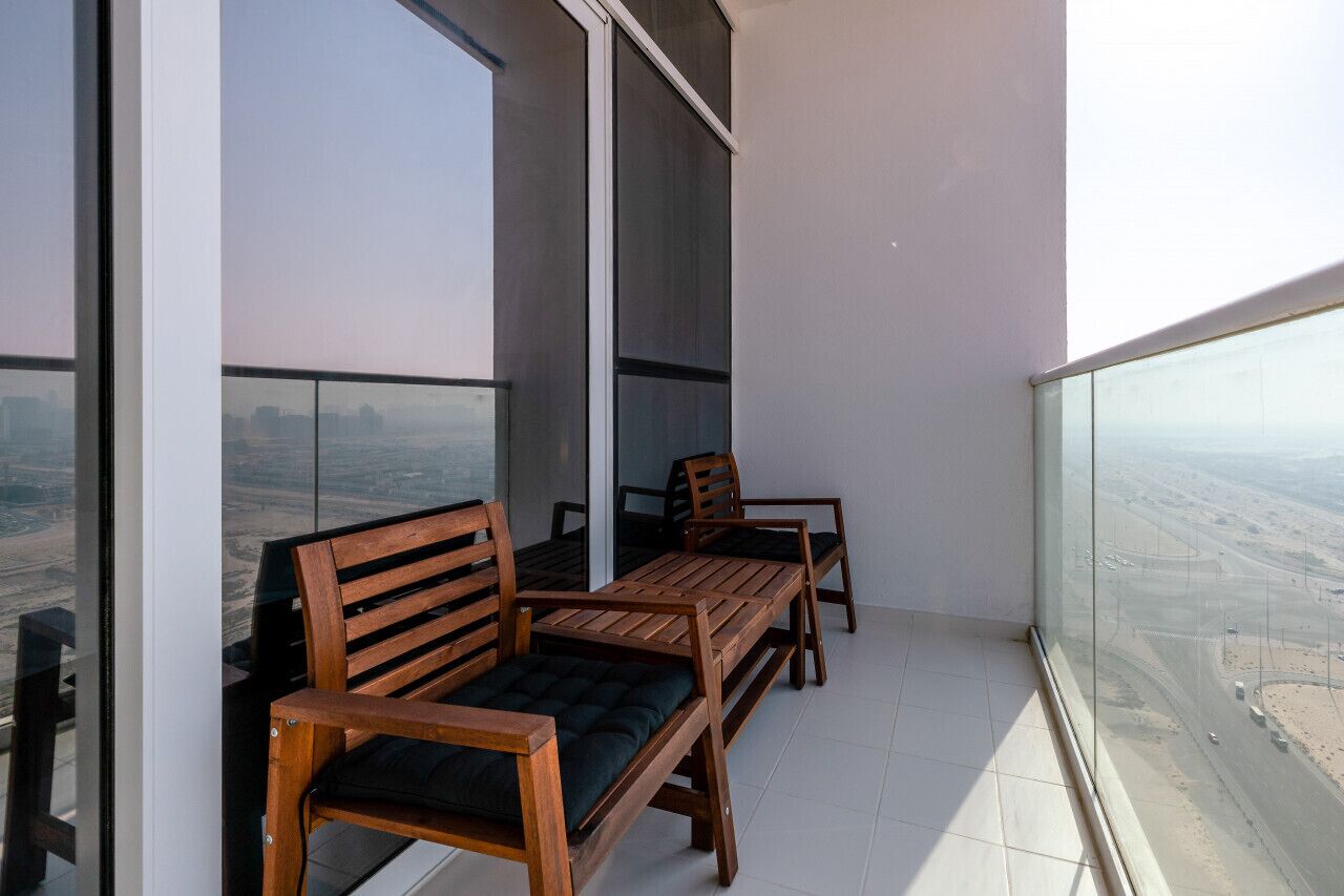 Ein Balkon mit einer Holzbänke und einem Tisch, großen Fenstern und Blick auf eine Wüstenlandschaft.