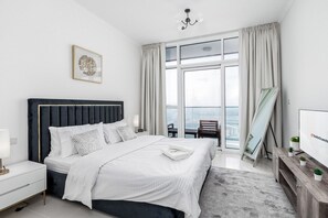 Ein modernes Hotelzimmer mit einem großen Bett, einem Nachttisch, einem Tischchen, einem Fernseher, einem Fenster mit Vorhängen und Blick auf die Stadt.