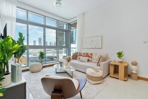 A modern living room with a large window, a sofa, a coffee table, and various decorative items. - Gala Guests - Iris Blue Living (Dubai)