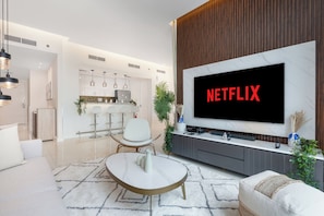 Ein modernes Wohnzimmer mit großem Flachbildfernseher, einem Essbereich und einer Küche im Hintergrund.