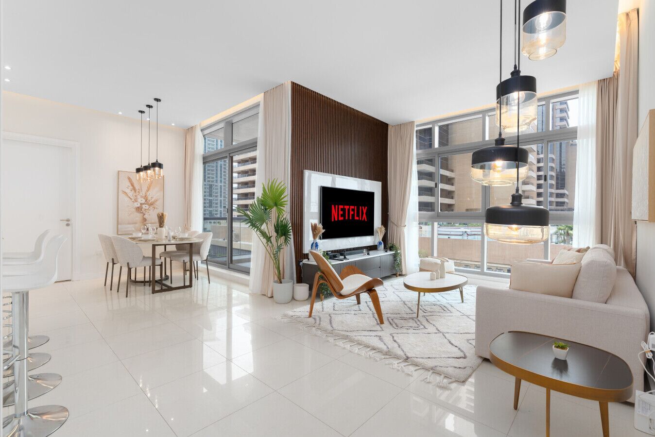 A modern living room with a TV displaying 'NETFLIX,' a dining area with a white table and chairs, and a sofa with a coffee table.