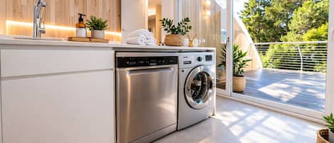 A modern kitchen with a built-in dishwasher and washing machine, wooden paneling, and a view of a balcony with plants.