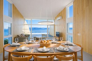 A dining area with a table set for six, a basket of bread, and a view of the sea through large windows. - Signature Lake View Luxury Residences M32 (San Carlos de Bariloche)