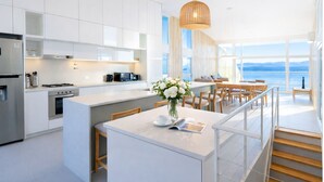 A modern kitchen with white cabinetry, a central island, and a dining area with a view of the sea. - Signature Lake View Luxury Residences M32 (San Carlos de Bariloche)