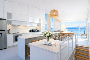 A modern kitchen with white cabinetry, a central island, and a dining area with a view of the sea. - Signature Lake View Luxury Residences M32 (San Carlos de Bariloche)