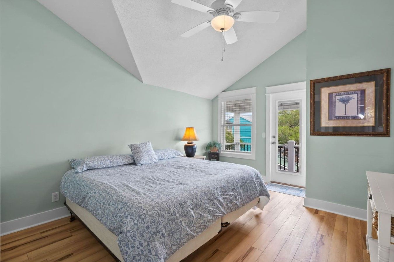 A bedroom with a bed, a ceiling fan, a nightstand with a lamp, and a window with blinds.