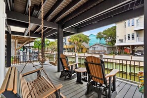 A covered outdoor area with wooden furniture, including a bench and chairs, overlooking a street with houses and a body of water. - Steps to Sand, Ocean Views, Water Park and Grill (Myrtle Beach)