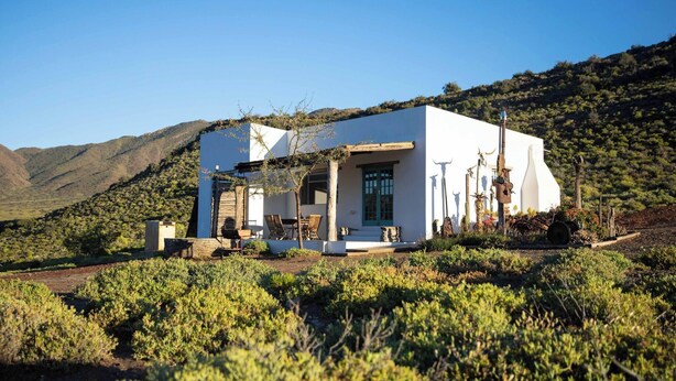 A white building with a patio, surrounded by vegetation and hills. - Tranquil Karoo Retreat (Laingsburg)
