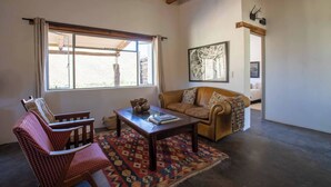 A living room with a sofa, armchair, coffee table, and a large window. - Tranquil Karoo Retreat (Laingsburg)