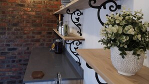 A kitchen with a brick wall, wooden shelves, a kettle, and a potted plant. - Tranquil Karoo Retreat (Laingsburg)