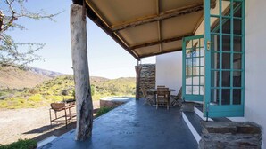A covered outdoor area with a table and chairs, a stone wall, and a turquoise door. - Tranquil Karoo Retreat (Laingsburg)
