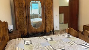 A bedroom with a wooden wardrobe, a bed with a patterned quilt, and a mirror.