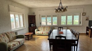 A dining area with a long table, chairs, a sofa, and a cabinet.