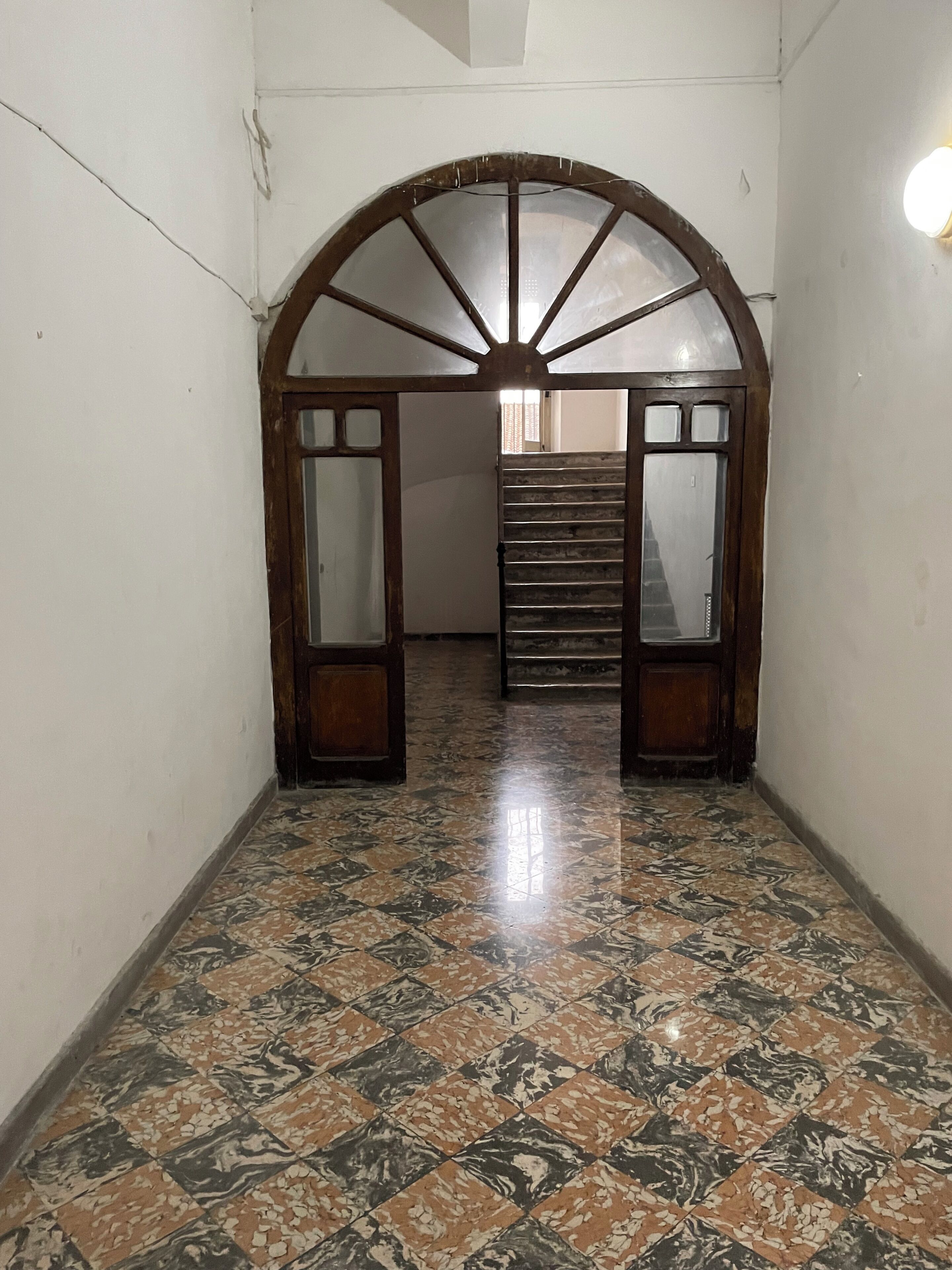 A hallway with a tiled floor, an arched doorway, and a staircase leading to another room.