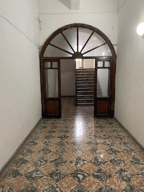 A hallway with a tiled floor, an arched doorway, and a staircase leading to another room.