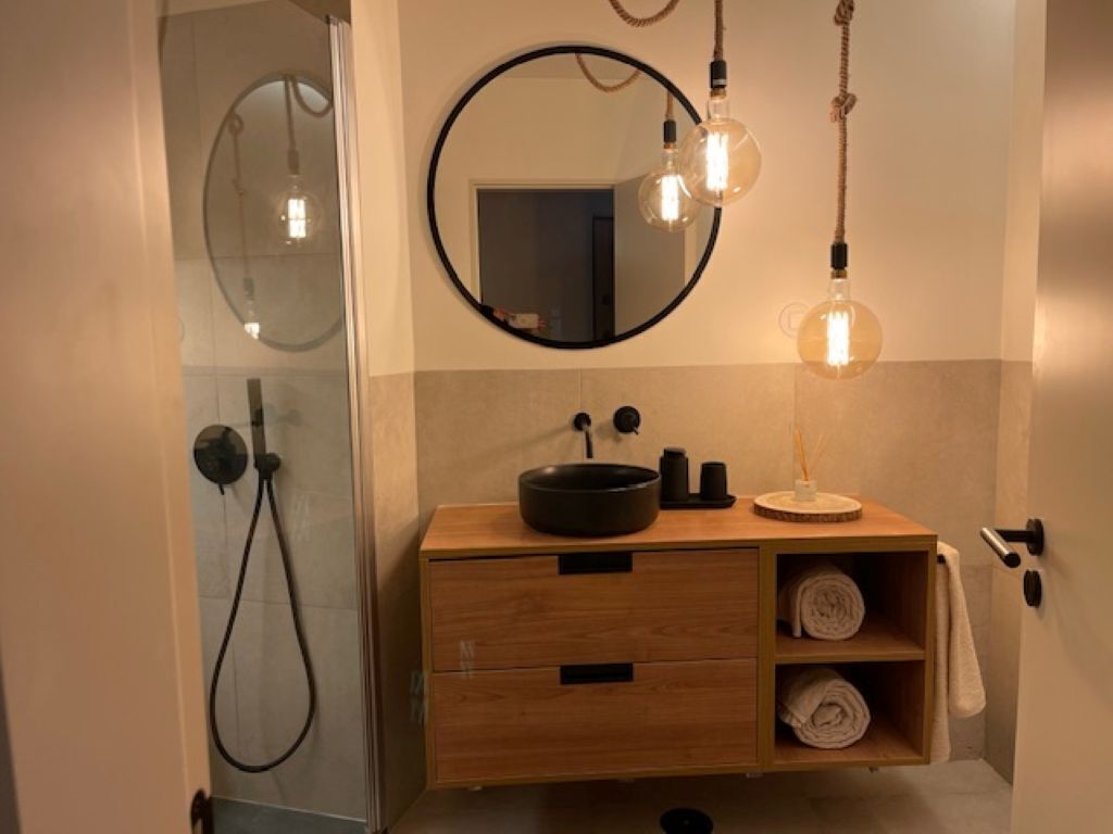 Un baño con tocador de madera, un espejo redondo, una lámpara redonda y un perchero para toallas.