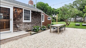 Une maison avec une façade en bois, une terrasse en gravier, une table avec des chaises et un petit jardin agrémenté d’hortensias.
