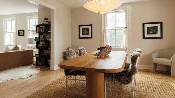 Un coin repas avec une table en bois, des chaises moelleuses, un luminaire suspendu et une bibliothèque en arrière-plan.
