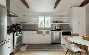 A modern kitchen with white cabinets, stainless steel appliances, and a dining area with a round table and wicker chairs. - 3-bedroom Gem on Main Street Sag Harbor Village (Sag Harbor)