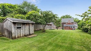 Un jardin avec un abri en bois, une pelouse et une maison en arrière-plan.