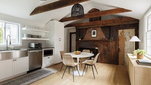 Une cuisine moderne avec des meubles blancs, un coin repas doté d’une table ronde et une cheminée en briques au style rustique.