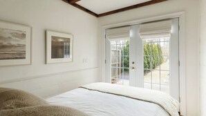 Une chambre à coucher avec un lit, une porte donnant sur un balcon et deux tableaux encadrés accrochés au mur.