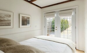 A bedroom with a bed, a door to a balcony, and two framed pictures on the wall. - 3-bedroom Gem on Main Street Sag Harbor Village (Sag Harbor)