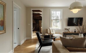 A living room with a sofa, a chair, a table, a TV, and a window. - 3-bedroom Gem on Main Street Sag Harbor Village (Sag Harbor)