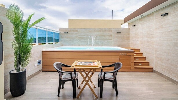 A modern outdoor area with a hot tub, wooden steps, a table with chairs, and a potted plant.