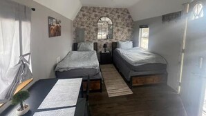 Ein Schlafzimmer mit zwei Betten, einem kleinen Tisch, einer Topfpflanze, einem Spiegel und einem Fenster.