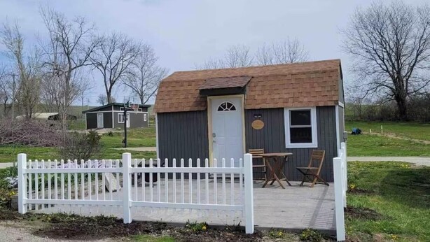 Ein kleines, eingeschossiges Blockhaus mit weißem Zaun, einer Tür und einem Fenster.