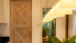 Una porta in legno con un motivo geometrico, una zona pranzo con tavolo e sedie, e una lampada a sospensione.