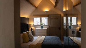 Una camera da letto con soffitto spiovente, un letto con testiera scura, comodini con lampade, una cassettiera e una finestra vista.