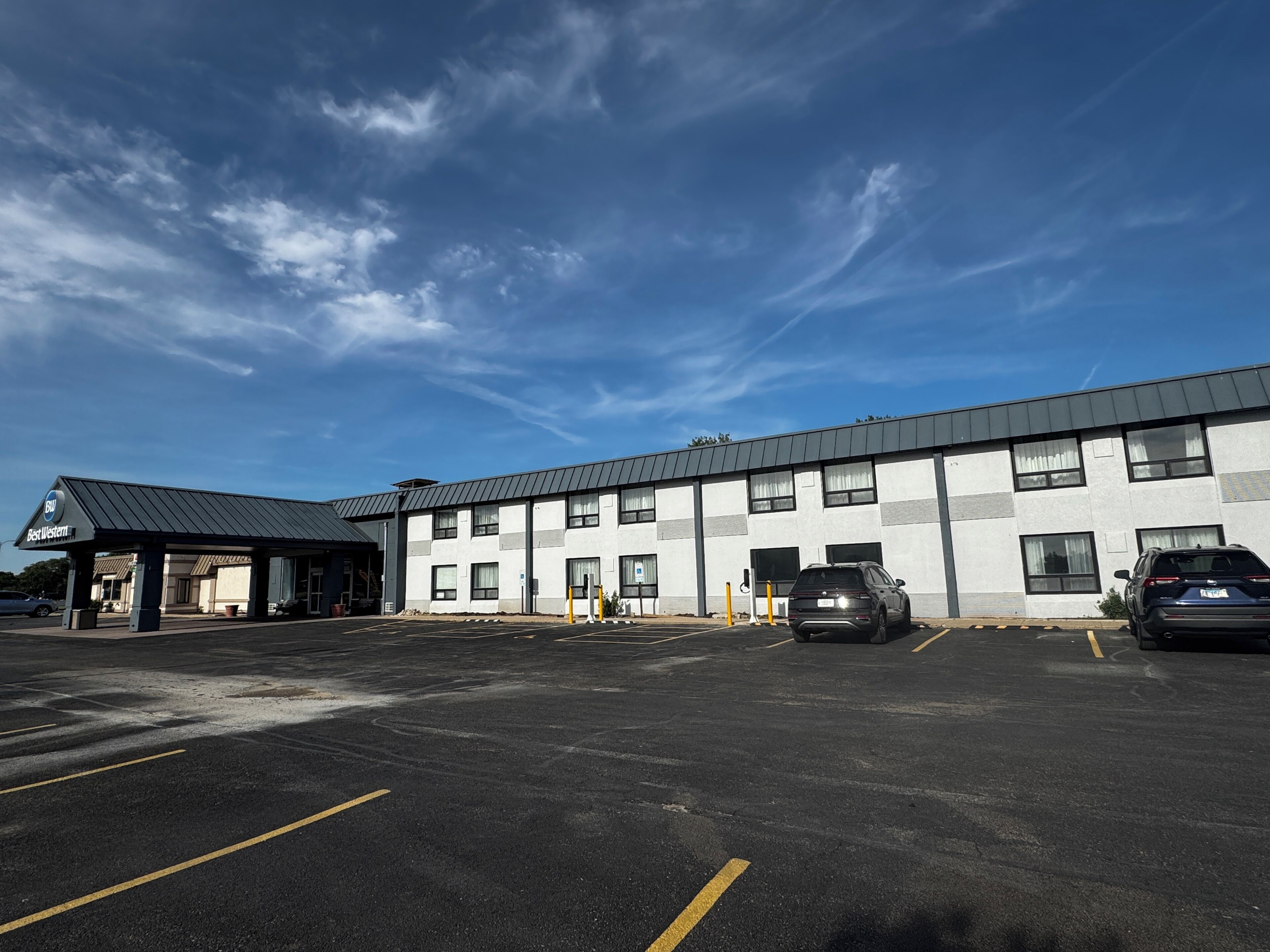 A building with a parking lot, a covered area, and a car parked in the lot.