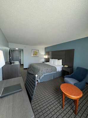 Quarto de hotel com uma cama, escrivaninha, cadeira, mesinha e televisão.