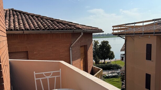 A balcony with a round table and chairs, a tiled roof, and a view of a body of water. - Lake house 40 minutes from Peschiera Del Garda, comfortably sleeps up to 4 people. (Mantova)