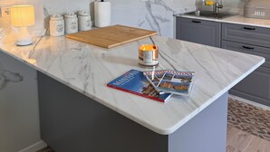 A modern kitchen with marble countertops, a central island, a wooden cutting board, a candle, and a magazine. - Lake house 40 minutes from Peschiera Del Garda, comfortably sleeps up to 4 people. (Mantova)