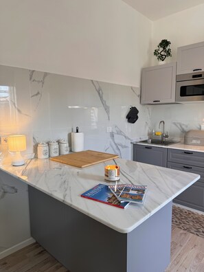 A modern kitchen with marble countertops, a central island, a wooden cutting board, a candle, and a magazine. - Lake house 40 minutes from Peschiera Del Garda, comfortably sleeps up to 4 people. (Mantova)
