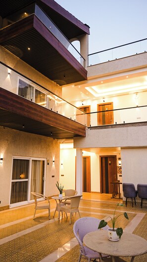 A multi-level building with a balcony, outdoor seating area, and a door leading to an interior space. - Ramana on the Ganges (Tapovan, Rishikesh)