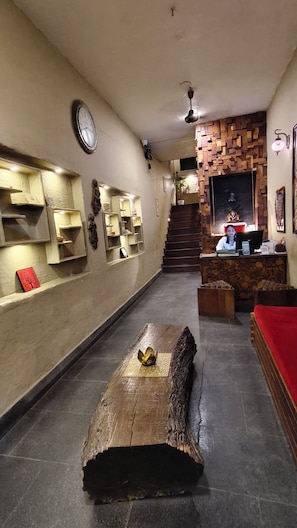 A reception area with a wooden reception desk, a clock on the wall, and a staircase leading to an upper level. - Ramana on the Ganges (Tapovan, Rishikesh)