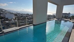 Una piscina a sfioro sul tetto con acqua cristallina, ampie finestre e vista sulla città e sull'oceano.