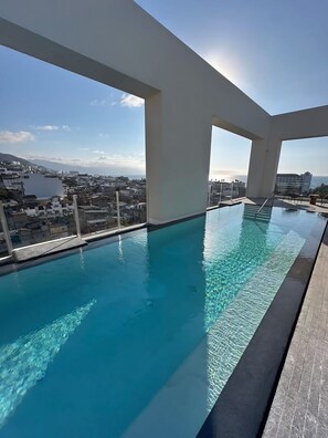 Ein Dachpool mit unendlicher Optik, klarem blauen Wasser, großen Fenstern und Blick auf Stadt und Meer.