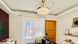 A modern living room with a black sectional sofa, a white entertainment unit, a chandelier, and a wooden door. - Private swimming pool in punta cana, electricity included (Punta Cana)