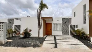 A modern two-story house with a central wooden door, stone accents, and a paved driveway. - Private swimming pool in punta cana, electricity included (Punta Cana)