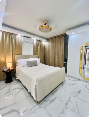 Ein Hotelzimmer mit Bett, Nachttisch, Lampe, Deckenventilator und Spiegel mit goldener Rahmung.