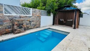 A swimming pool with stone walls, a covered seating area, and a modern building with large windows. - Private swimming pool in punta cana, electricity included (Punta Cana)