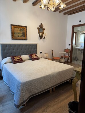 A bedroom with a large bed, a chandelier, a framed painting, and a bathroom visible through an open door. - Ca Pierre (Venice)